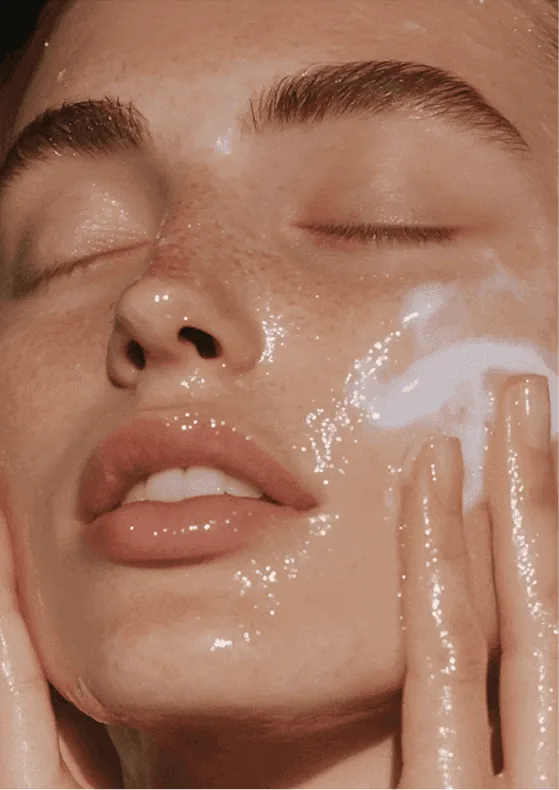 Mulher de olhos fechados aplicando creme no rosto.