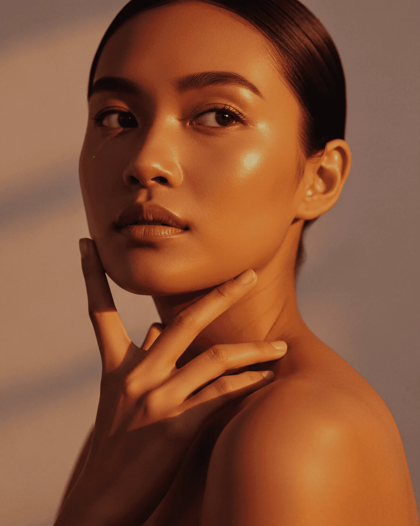 Mulher com a mão apoiada no queixo, pele hidratada em luz quente.